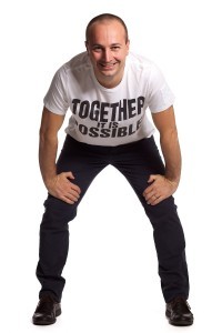 A professional studio photo of a man in a white space wearing black pants and a T-shirt that says "together it is possible"